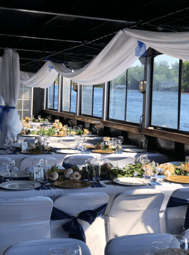 Decorated event space with white linens, navy sashes, and a waterfront view, decor by Decorentals2go Ottawa